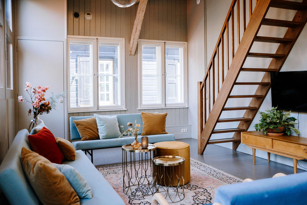 Groepsaccommodatie D2 voor 8 personen Woonkamer met banken, bijzettafels en trap naar verdieping